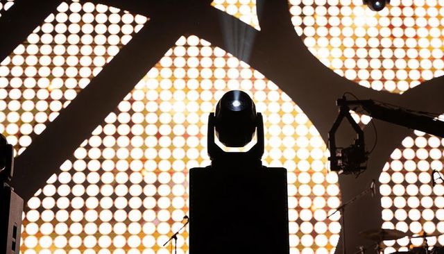 Moving spotlight silhouetting center stage against led dot matrix backdrop and rigging