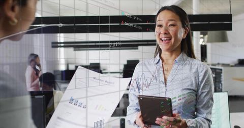 Smiling businesswoman presenting digital data on tablet in modern office with financial charts
