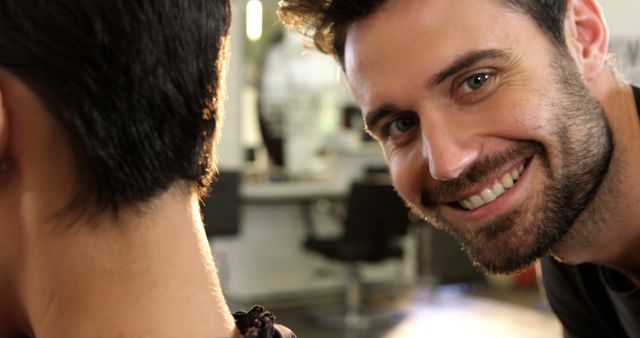 Shows a smiling barber interacting with a client in a modern hair salon. Ideal for use in advertisements for hair salons, grooming services, professional training, and customer service promotions. Emphasizes positive customer experiences, professional service, and modern business environments.