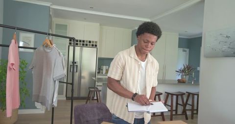 Young african american man writing notes and planning wardrobe in modern open-plan kitchen