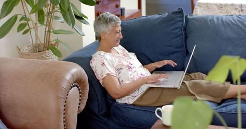 Senior Woman Relaxing on Couch Using Laptop At Home, Embracing Technology