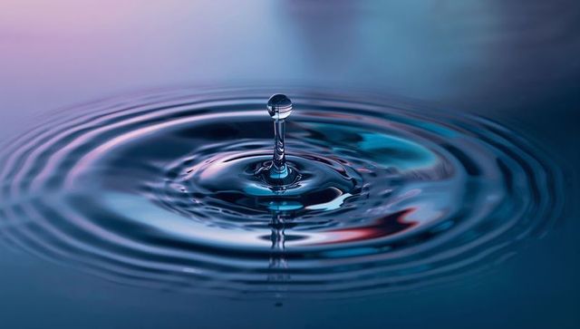 Macro water droplet rebounding on vertical jet with ripples and teal-magenta reflections