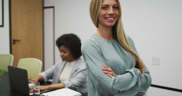 Portrait of caucasian businesswoman smiling in office, with colleague working in background. work at an independent creative business.