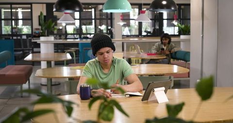 African american man studying in coworking space writing notes while using tablet stand