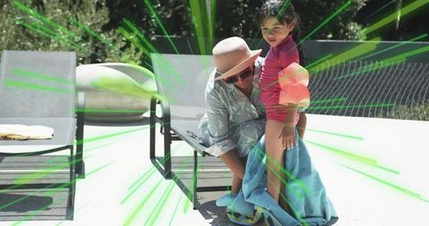 Mother adjusting towel around daughter at sunny pool deck with sun hat and floaties