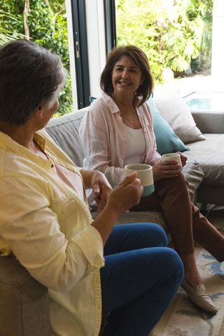 Senior Women Having Relaxing Coffee Chat by Glass Door