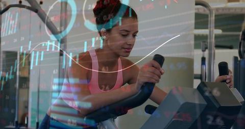Young woman pedaling on stationary bike with stock market charts overlay