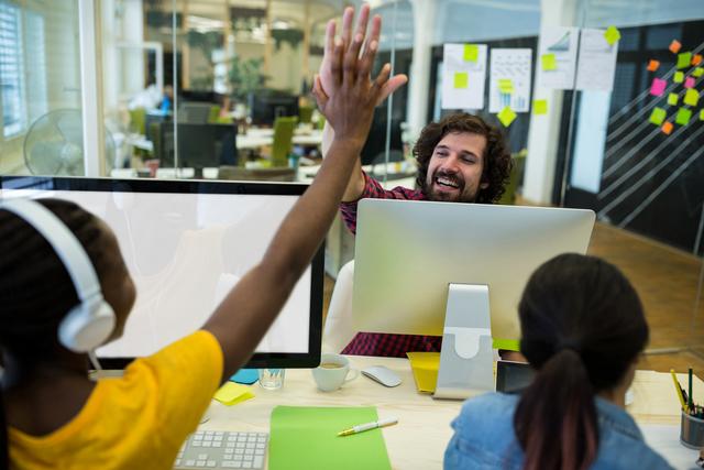 Male graphic designer giving high five to his coworker in office