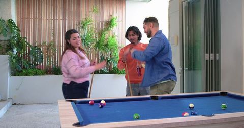 Friends playing pool on blue felt table at leafy covered patio social game night