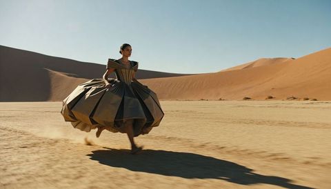Couture gown sprinting across sunlit desert dunes, sculptural geometric dress motion