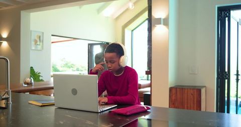 African american father supervising son studying on laptop in modern open-plan kitchen