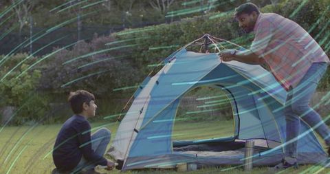 Father and son assembling backyard tent at dusk for family outdoor camping and bonding