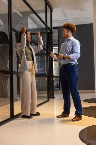 Diverse coworkers celebrating success through glass divider in modern corporate office