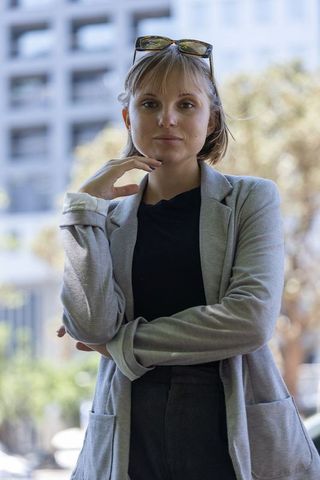 Confident young professional posing in city wearing light-gray blazer, sunglasses on head