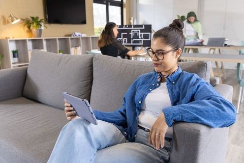 Diverse women collaborating in modern coworking lounge, reviewing tablet and floor plan