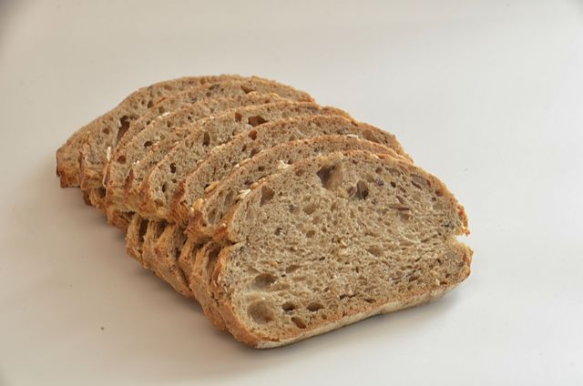 Rustic multigrain bread sliced and displayed on a white background. Showcasing the texture and grains within the loaf. Suitable for use in food blogs, recipe websites, advertisements for bakeries, or health-related articles emphasizing wholesome eating.