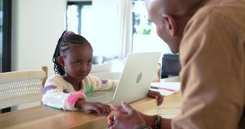 African american child learning on laptop with caregiver at home, family tech bonding