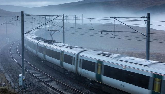 Electric commuter train rounding foggy moorland curve with overhead catenary motion blur