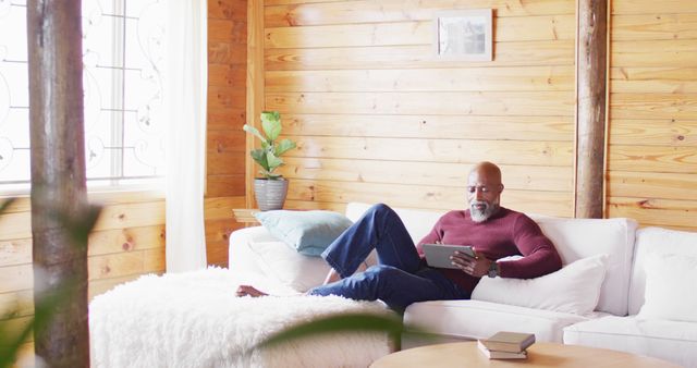 Mature Man Relaxing on Sofa Using Tablet in Cozy Wooden Cabin - Download Free Stock Images Pikwizard.com