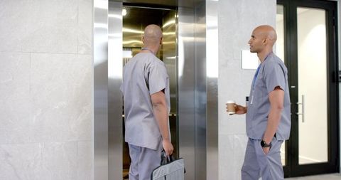 African american medical staff in scrubs waiting by elevator holding coffee and briefcase