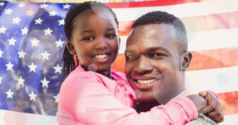 African American Soldier Holding Daughter in Front of Flag