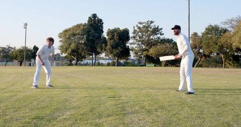 Two men playing cricket on grassy park field at golden hour, batsman ready with bat