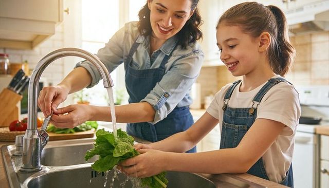 Mother and daughter washing lettuce together in bright home kitchen