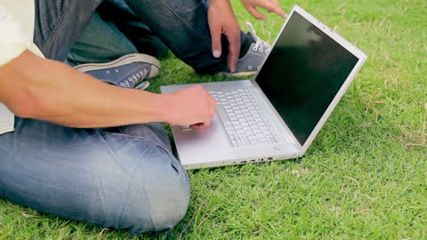 Individual sitting on grass in park using laptop. Suitable for themes of remote work, digital freedom, technology, and outdoor leisure. Ideal for articles on flexible work environments or illustrating park amenities.