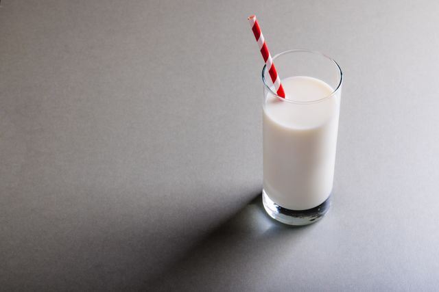 High angle view of a glass of milk with a red striped straw on a gray background. Ideal for promoting healthy eating, dairy products, or minimalist designs. Suitable for use in advertisements, health blogs, and nutrition articles.