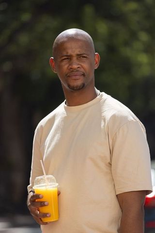 Thoughtful man holding cold orange juice cup outdoors on sunny street in casual tee