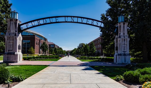 Visual of Purdue University's iconic archway entrance with a sunny sky and green campus, providing an inviting scene. Ideal for marketing educational programs, alumni material, and promoting higher education institutions.