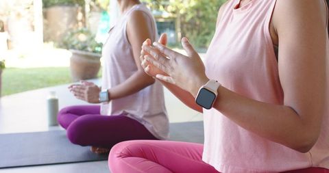 Diverse women meditating outdoors on patio mats in bright leggings wearing smartwatches