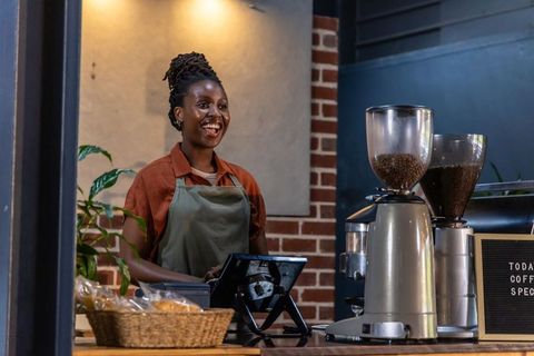 African american barista smiling behind counter serving coffee in cozy rustic cafe interior