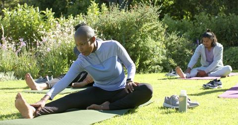 Diverse group practicing outdoor yoga and stretching on sunny lawn with mats and sneakers