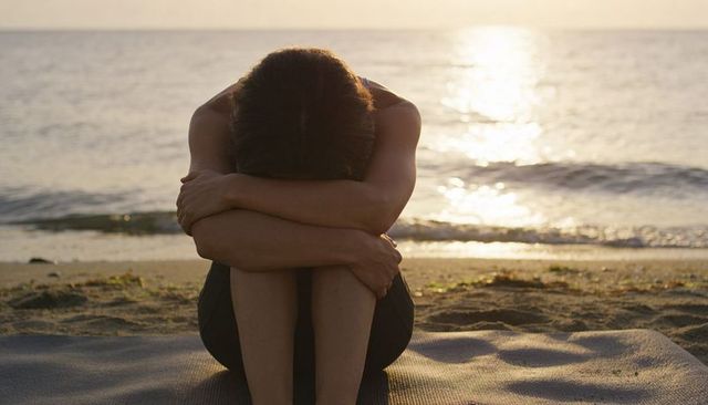 Woman sitting hugging knees on beach at sunset reflecting solitude and calm at shoreline