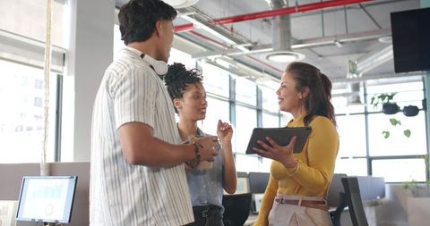 Diverse young professionals collaborating with tablet and coffee in modern open-plan office