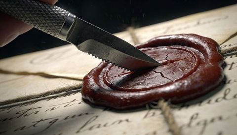 Serrated knife cutting red wax seal on antique handwritten parchment, closeup detail