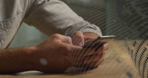 Holding and tapping smartphone on wooden desk with dotted glass reflection and warm light