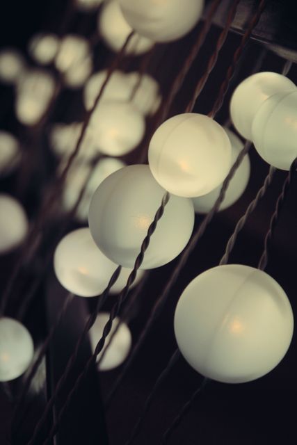 Softly glowing string of white bulbs creating moody and calm ambiance with dark background in focus. Ideal for use in designs related to home decor, cozy or intimate settings, nighttime events, romantic themes, relaxation environments, or holiday decoration inspirations.