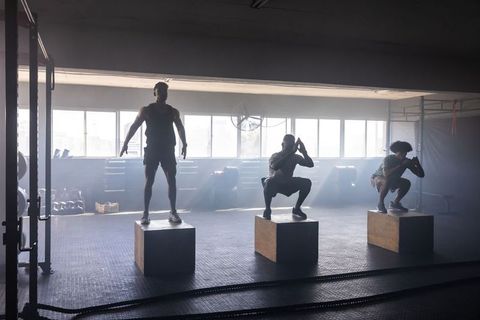 Diverse athletic group performing intense squat jumps in gym