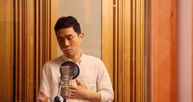Young man singing in professional recording studio, showing emotion while holding microphone. Perfect for content about music production, performance, creative process, vocal training, recording artist promotion.
