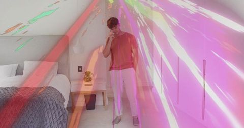 Young man standing in loft bedroom talking on phone with neon light projection overlay