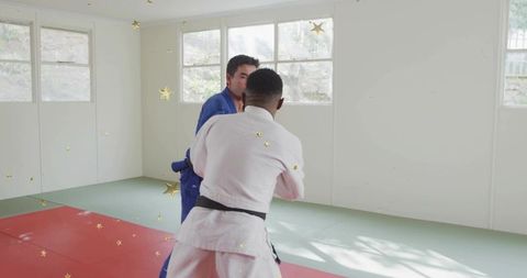 Judokas sparring on tatami mats by sunlit windows wearing blue and white gis