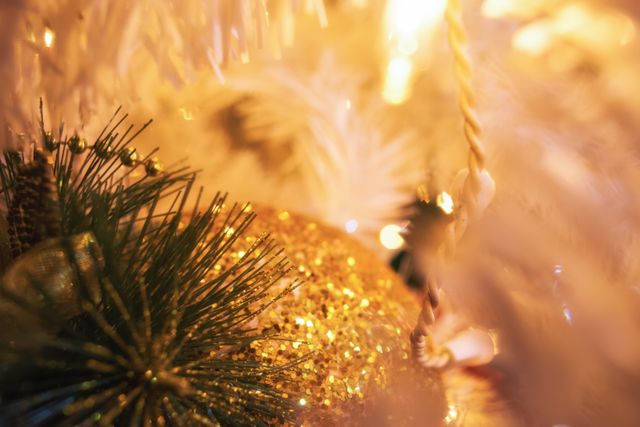 Glittering gold Christmas ornament nestled among green pine needles and white decorations. Ideal for holiday greeting cards, festive background images, blog posts about Christmas decor, and advertising seasonal products.