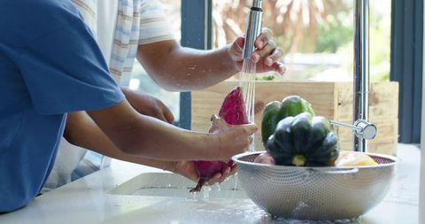 African american father and son rinsing yam under kitchen faucet preparing healthy meal