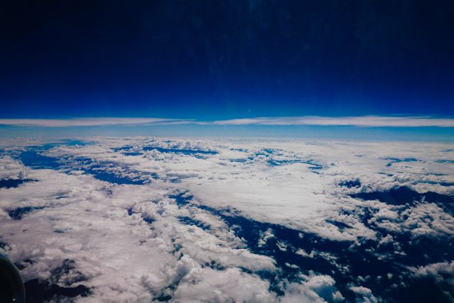 Beautiful aerial view capturing a sea of fluffy clouds with a clear horizon and vibrant blue skies. Useful for travel, aviation, and nature-themed projects, backgrounds and promotions emphasizing tranquility and scenic views.