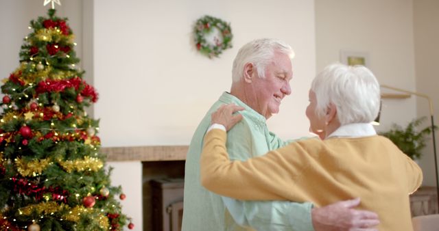 Elderly couple dancing joyfully near Christmas tree with holiday decorations. This joyful image could be used for Christmas and holiday promotions, senior living content, and advertising celebrating family life and togetherness.