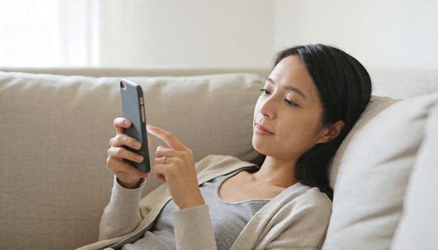 Relaxing woman scrolling smartphone on beige sofa, cozy minimal home lifestyle moment