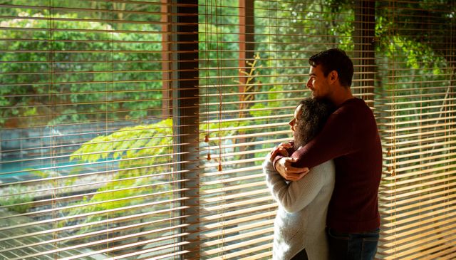 Diverse couple standing at window and embracing at home. enjoying free time in luxury rural home.