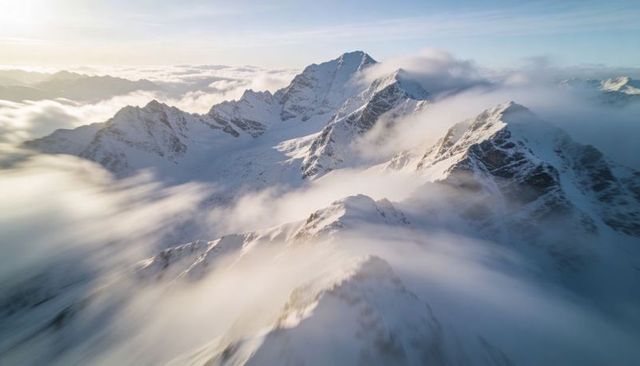 Sunlit jagged alpine peak with drifting clouds, snow-covered ridges and dramatic panorama